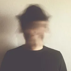 A blurred face of a man wearing a black hat and black shirt, indicating psychiatric instability.