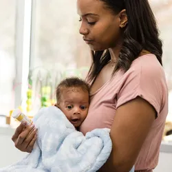 A female clinician gestures as she explains the dosage and side effects of a medication to a worried young mother holding a baby.