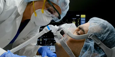 A female clinician checks on a patient connected to a ventilator in a hospital room.