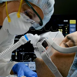 A female clinician checks on a patient connected to a ventilator in a hospital room.