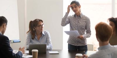A nervous female employee/presenter/speaker stands in front of multi-ethnic colleagues/clients in a business meeting