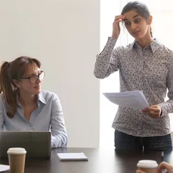 A nervous female employee/presenter/speaker stands in front of multi-ethnic colleagues/clients in a business meeting