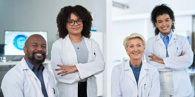 Close up of one male and three female clinical researchers wearing lab aprons and smiling in a laboratory