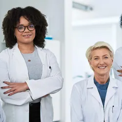 Close up of one male and three female clinical researchers wearing lab aprons and smiling in a laboratory