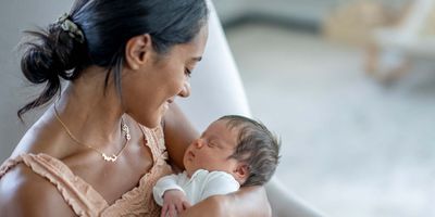 A new mother looks at and rocks her baby gently in her arms while sitting in the nursery.