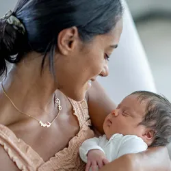 A new mother looks at and rocks her baby gently in her arms while sitting in the nursery.