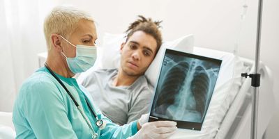 A female clinician explain a lung X-ray report to a male patient lying on the bed in a hospital room.