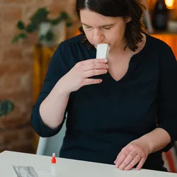 A woman spits into a saliva collection pouch as she prepares to examine her blood.