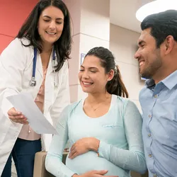 A female clinician shows a smiling pregnant couple a sheet of paper in an office.
