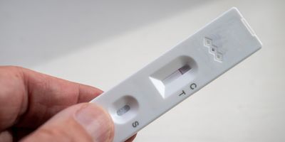 A person holding a rapid, at-home lateral flow test strip with wells for a sample and the biosensor.