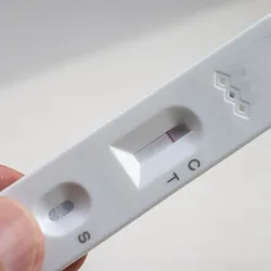 A person holding a rapid, at-home lateral flow test strip with wells for a sample and the biosensor.