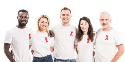 A multiethnic group of men and women in white t-shirts and jeans wear red ribbons in support of HIV-AIDS awareness.