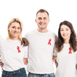 A multiethnic group of men and women in white t-shirts and jeans wear red ribbons in support of HIV-AIDS awareness.