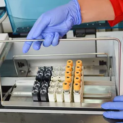 A pair of gloved hands set a rack of blood vacutainers for testing in a piece of equipment.