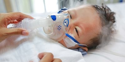 A caregiver puts on a nebulization mask on an infant with a respiratory infection in a hospital setting.