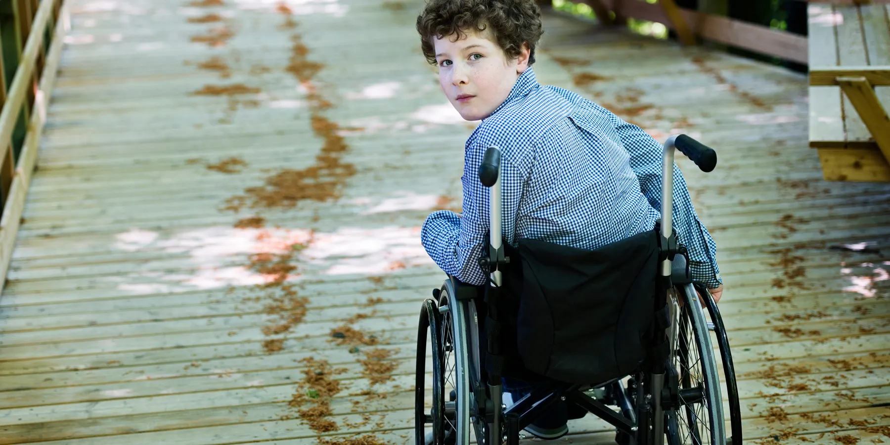 A young boy in a wheelchair looks back into the camera.