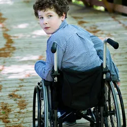 A young boy in a wheelchair looks back into the camera.