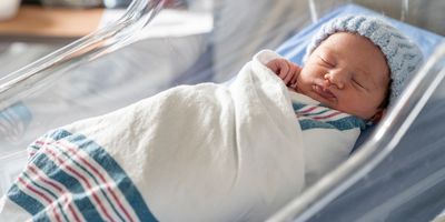 A newborn baby swaddled and in a beanie in the hospital cradle.