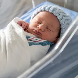 A newborn baby swaddled and in a beanie in the hospital cradle.