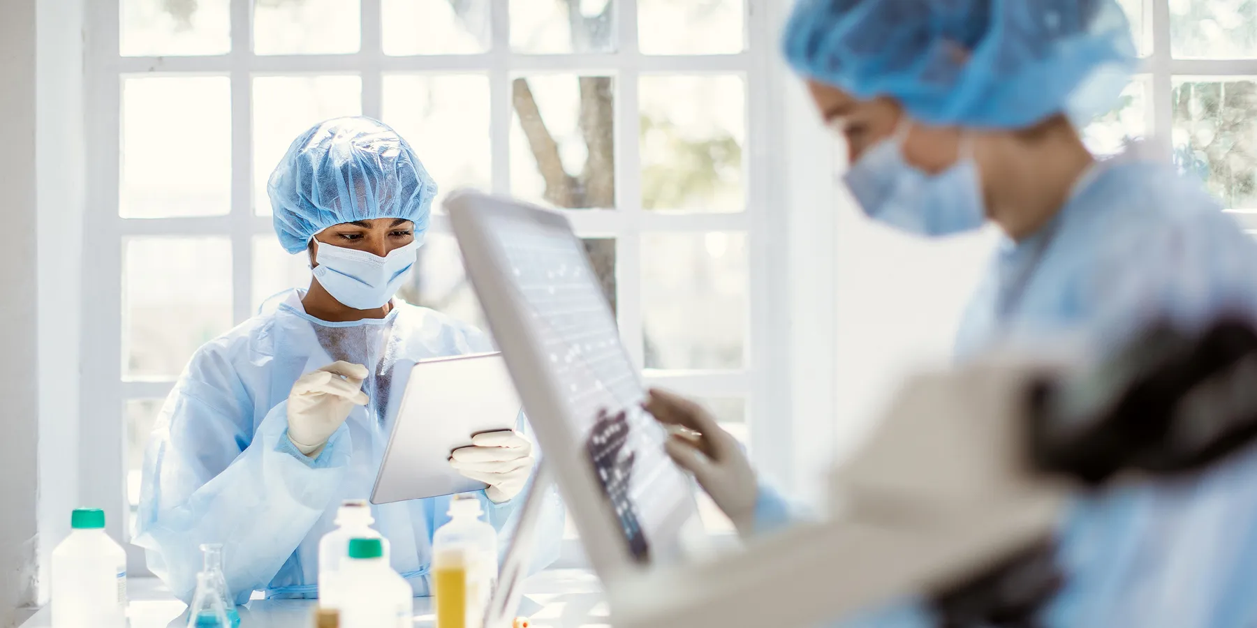 Two female researchers in PPE work on digital tablet and touch-screen computer interface in a  lab setting.
