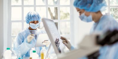 Two female researchers in PPE work on digital tablet and touch-screen computer interface in a  lab setting.