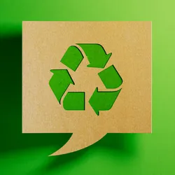 Photo of a chat bubble made from cardboard with a cut-out in the shape of a recycling symbols with three arrows on a green background.