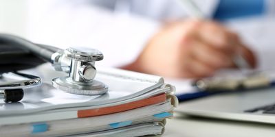 Photo of a stethoscope resting on top of a pile of medical records in a clinician’s office.