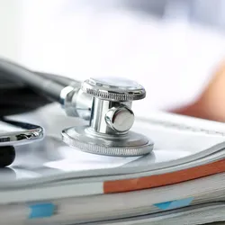 Photo of a stethoscope resting on top of a pile of medical records in a clinician’s office.