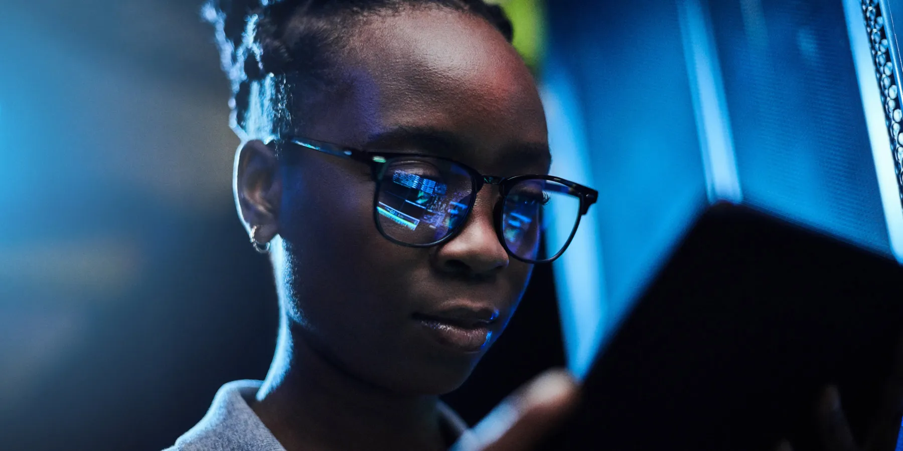 Photo of a young Black female artificial intelligence engineer using a digital tablet while working in a dark computer server room.