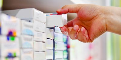 Photo of a person’s hand reaching for an item on the shelf of a pharmacy. 