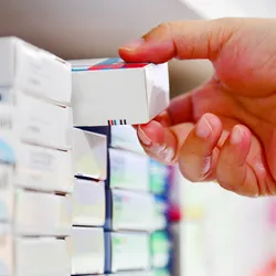 Photo of a person’s hand reaching for an item on the shelf of a pharmacy.