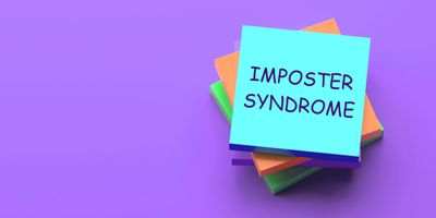 Photo of a pile of sticky notes on a purple background with the top sticky note reading “imposter syndrome.”