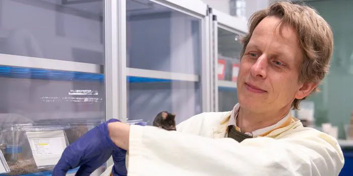 Photo of associate professor Martin K. Thomsen wearing a white lab coat in the lab with a mouse on his arm.