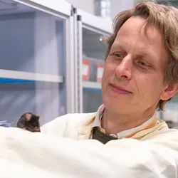 Photo of associate professor Martin K. Thomsen wearing a white lab coat in the lab with a mouse on his arm.