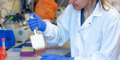Photo of a clinical laboratory professional wearing PPE in the lab and holding a multichannel pipette.
