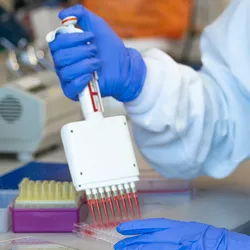 Photo of a clinical laboratory professional wearing PPE in the lab and holding a multichannel pipette.