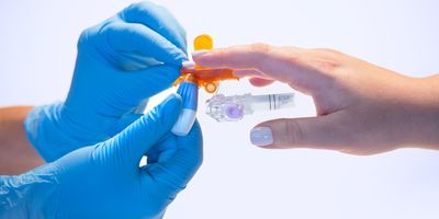 Photo of a technician holding a patient's hand and taking a sample of blood in the BD MiniDraw