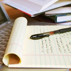 Open laptop with note pad and pen on top