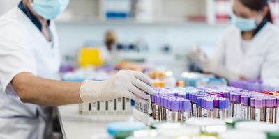 Photo of two medical laboratory professionals wearing PPE in a clinical lab processing blood sample tubes.