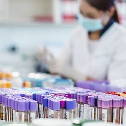 Photo of two medical laboratory professionals wearing PPE in a clinical lab processing blood sample tubes.