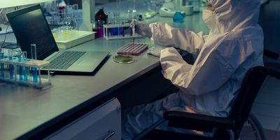 Photo of a clinical laboratory professional wearing PPE using a wheelchair at the laboratory bench.