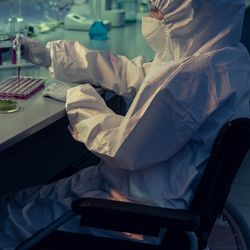 Photo of a clinical laboratory professional wearing PPE using a wheelchair at the laboratory bench.