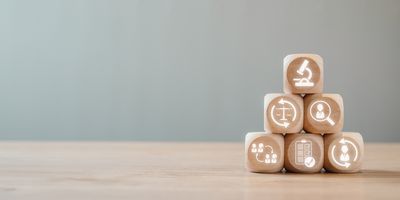 Photo of wooden blocks stacked in a pyramid with symbols related to the clinical laboratory carved into the fronts.