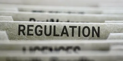 Photo of the word “regulation” in bold capital letters on the side of a file folder.