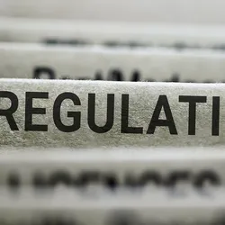 Photo of the word “regulation” in bold capital letters on the side of a file folder.