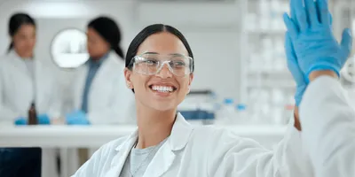 Photo of a smiling clinical laboratory professional wearing PPE in the lab giving a high five to another laboratorian.