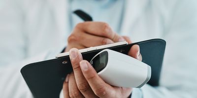 Photo of a clinical researcher wearing PPE holding a clipboard and a pen to fill out a research study form guidelines.