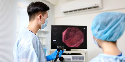 Photo of a clinical technician wearing PPE examining a colonoscopy on a monitor in a clinic.