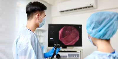 Photo of a clinical technician wearing PPE examining a colonoscopy on a monitor in a clinic.
