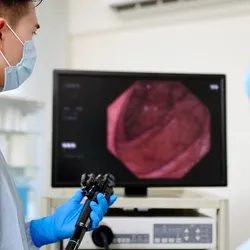 Photo of a clinical technician wearing PPE examining a colonoscopy on a monitor in a clinic.